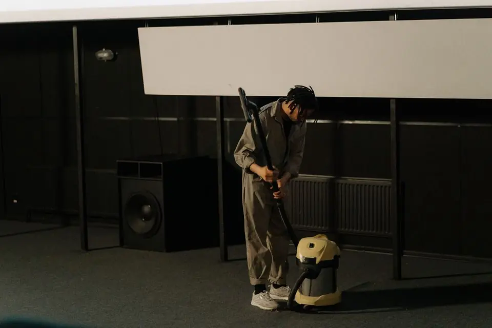 A Man Holding a Vacuum Cleaner near a Speaker